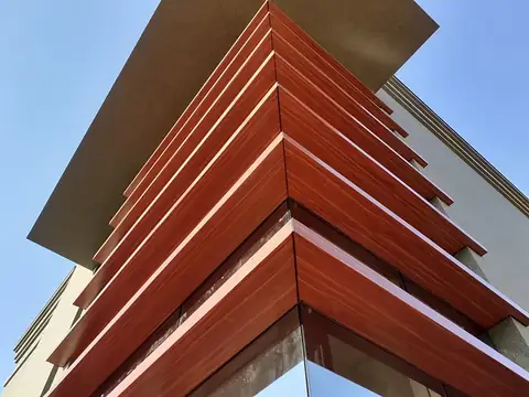 Revestimento em ACM com acabamento amadeirado em lâminas escalonadas na quina de um prédio, visto de baixo