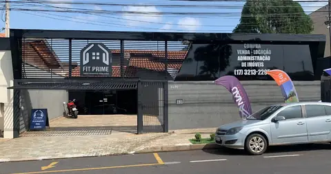 Fachada em ACM preto com logo vazado da Fit Prime e painel de venda e locação de imóveis