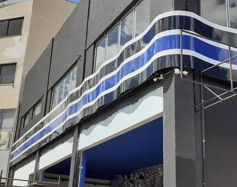 Faixa ondulada em ACM azul e branco contornando o andar superior de um prédio comercial