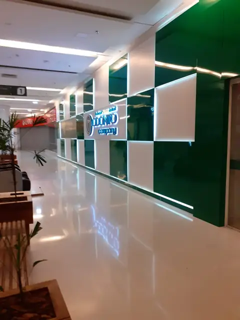 Corredor interno de shopping com painéis verdes e brancos e letreiro iluminado ao fundo