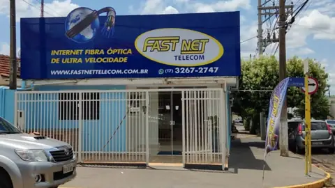 Fachada em ACM azul com impressão da Fast Net Telecom e informações de internet fibra óptica