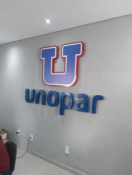 Logo em letras caixa da Unopar, azul e vermelho, aplicado em parede cinza de sala interna