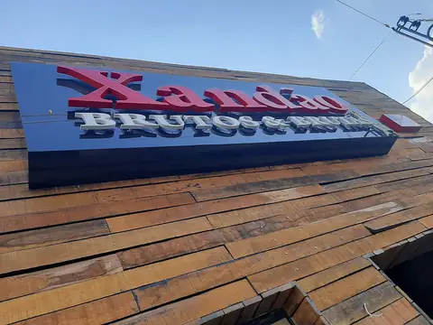 Letreiro com letras caixa vermelhas e cinza sobre fundo azul, em fachada de madeira, visto de baixo