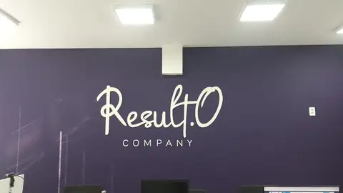Letras caixa brancas em fonte manuscrita da Result.O Company sobre parede roxa de recepção