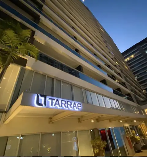 Letras caixa iluminadas da Tarraf na entrada de um edifício, fotografadas ao entardecer
