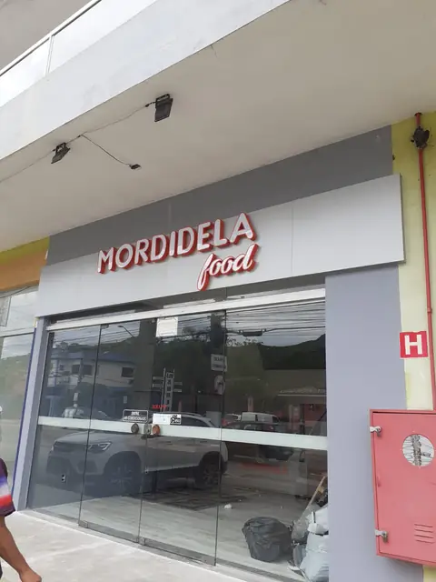 Letras caixa vermelhas da Mordidela Food sobre fachada cinza com portas de vidro