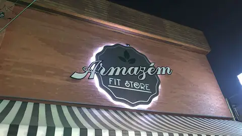 Logo recortado com retroiluminação da Armazém Fit Store em parede de tijolos, à noite