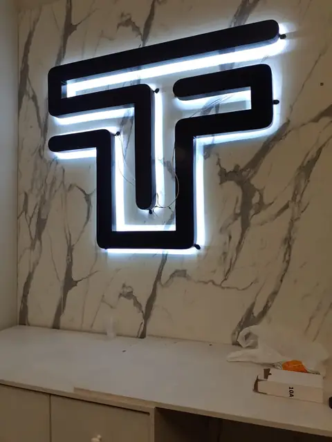 Letra T vazada em preto com retroiluminação em LED branco sobre parede de mármore