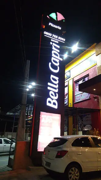 Totem alto iluminado da pizzaria Bella Capri com letras brancas, à noite