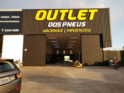 Letras caixa amarelas da Outlet dos Pneus sobre fachada de chapa escura, ao fim da tarde