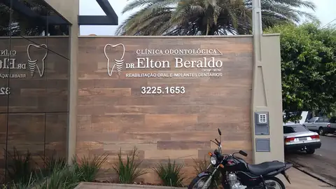 Muro revestido de madeira com letras e logo de dente da Clínica Odontológica Dr. Elton Beraldo