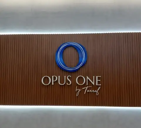 Logo azul vazado e letras da Opus One by Tarraf sobre painel ripado de madeira com LED