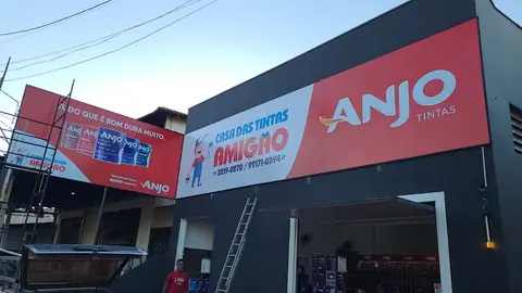 Fachada em lona impressa vermelha e cinza da Casa das Tintas Amigão com marca Anjo Tintas