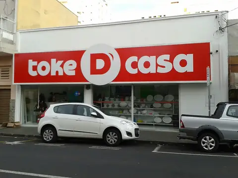 Fachada com letreiro vermelho e letras brancas da Toke D Casa sobre prédio branco