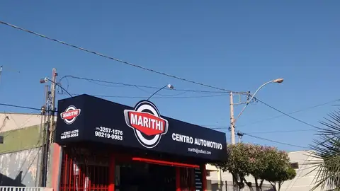 Placa impressa azul e vermelha do Centro Automotivo Marithi sobre fachada com grade vermelha