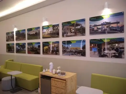 Sala de espera com quadros de fotos de empreendimentos em acrílico na parede branca, sofá verde-limão