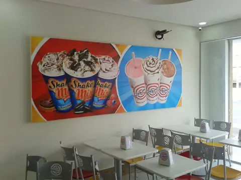 Painel impresso de milk-shakes coloridos em parede de lanchonete com mesas brancas