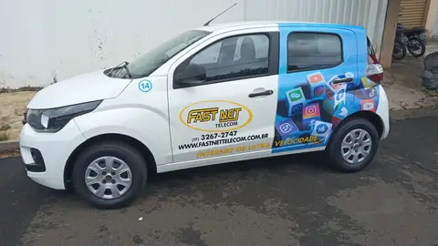 Carro compacto branco com adesivo da Fast Net Telecom e ícones de redes sociais em azul na traseira