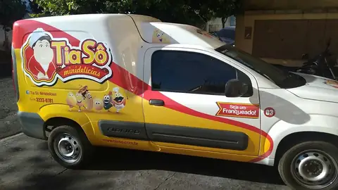 Utilitário branco com envelopamento amarelo e vermelho da Tia Sô minidelícias, personagem na porta