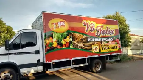 Caminhão baú com adesivo impresso de frutas e verduras do supermercado Vô Felix, fundo vermelho