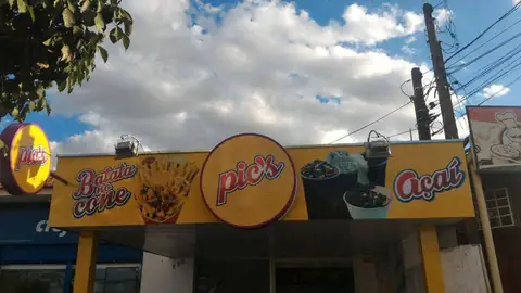 Fachada amarela da Pic's com logotipos redondos de batata, açaí e lanche, sob céu nublado