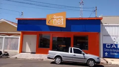 Fachada em ACM azul e laranja com letreiro luminoso Guaptel net, picape prata em frente