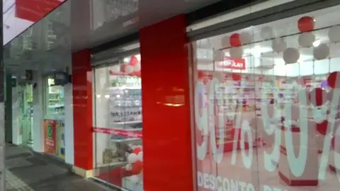 Fachada de farmácia com colunas e faixa em ACM vermelho e vidro com adesivos de desconto