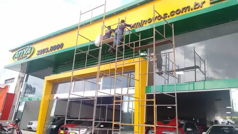 Fachada em ACM verde e amarelo da Atiya com pórtico amarelo, instaladores em andaime