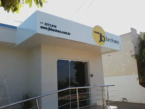 Fachada branca com letreiro redondo amarelo jb bechara e telefone, entrada com corrimão inox