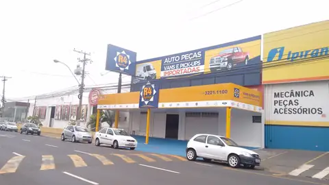 Fachada de auto peças com painel amarelo e azul R4, ilustrações de picapes, rua com faixas