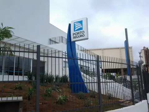 Totem azul curvo com logotipo Porto Seguro em frente a prédio branco com grade preta