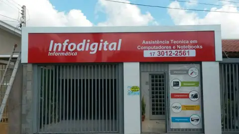 Painel vermelho Infodigital Informática com telefone 3012-2561 sobre fachada com portão de grade