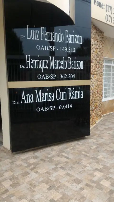 Placa preta polida com nomes e registros OAB de três advogados ao lado de entrada com piso cerâmico
