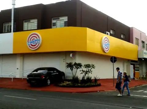 Fachada de esquina em ACM amarelo com dois logotipos circulares Chiquinho, calçada vermelha
