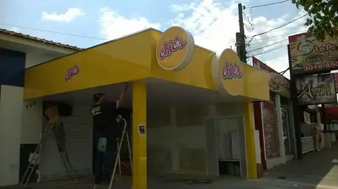 Fachada em ACM amarelo com logotipos redondos Chic's, instalador em escada