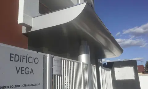 Marquise curva em ACM prateado sobre portaria com placa Edifício Vega, vista de baixo