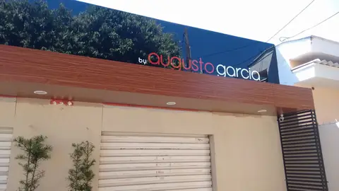 Fachada com ACM amadeirado e letras Augusto Garcia sobre painel azul, portão de enrolar