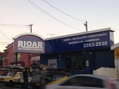Fachada azul com letreiro Rioar Ar Condicionado e telefone 3353-2530 ao entardecer