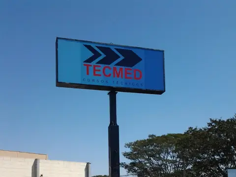Painel luminoso azul da Tecmed em poste alto, com setas e letras vermelhas contra o céu