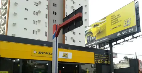 Fachada amarela da B2 Pneus com letras Dunlop e outdoor amarelo acima