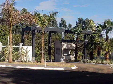 Pórtico escuro com pergolado e guarita entre palmeiras, entrada de condomínio