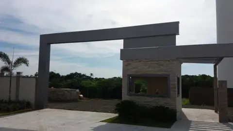 Pórtico em ACM cinza sobre guarita com revestimento de pedra, fundo de mata