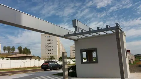 Pórtico em ACM cinza com pergolado sobre guarita branca, céu azul com nuvens