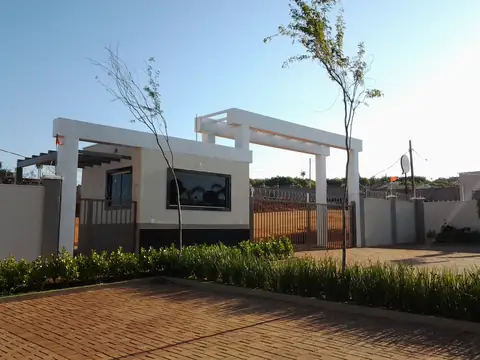 Pórtico branco com pergolado sobre guarita, piso de pavers e jardim na frente