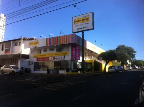 Prédio de esquina com totem em poste e faixas coloridas na fachada da Idiom Center, céu azul