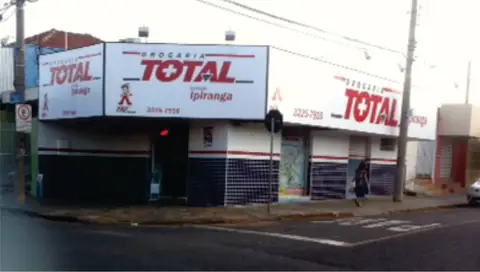 Esquina com caixas luminosas brancas e vermelhas da Drogaria Total Ipiranga