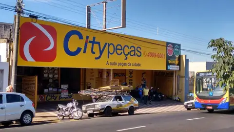 Grande fachada amarela da Citypeças com logo azul e vermelho, ônibus passando ao lado
