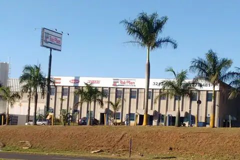 Totem alto em poste e faixa de letreiros ao longo de prédio comercial, entre palmeiras
