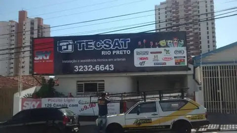 Fachada com painel preto da Tecsat Rio Preto e faixas da Sky, carro adesivado na frente