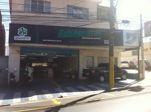 Fachada preta da Luk Martin, máquinas de costura, com letras verdes e logo à esquerda